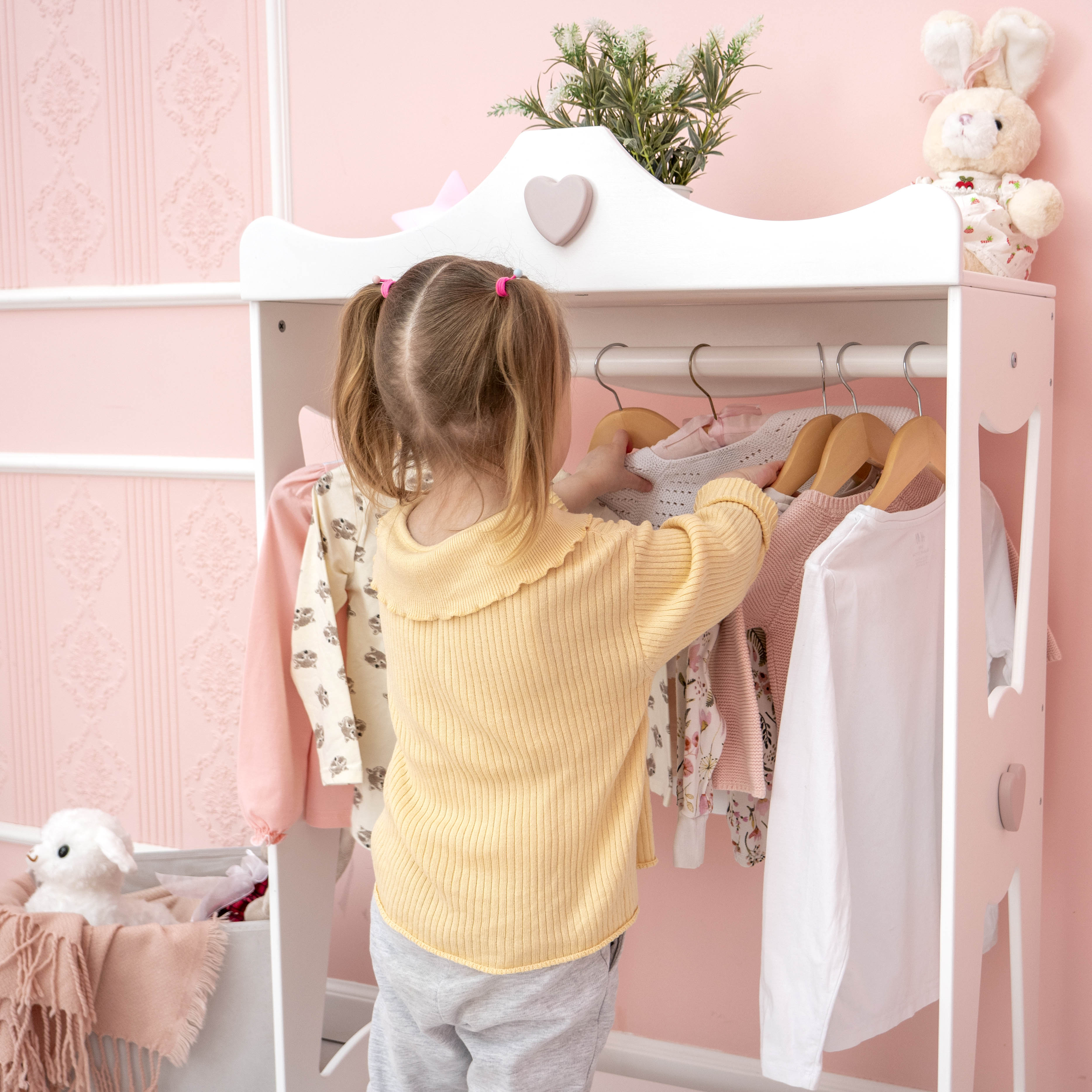 Cute little girl choosing festive dress hanged in pink cupboard